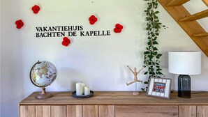 Un meuble en bois orné d’un globe terrestre, de bougies, d’un cadre photo et d’un mur décoré de coquelicots rouges, sur lequel on peut lire l’inscription « VAKANTIEHUIS BACTEN DE KAPELLE ».
