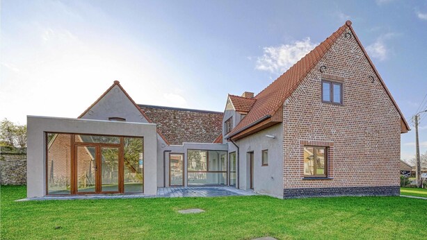 Une maison moderne avec une façade en briques, de grandes fenêtres et une pelouse bien entretenue.