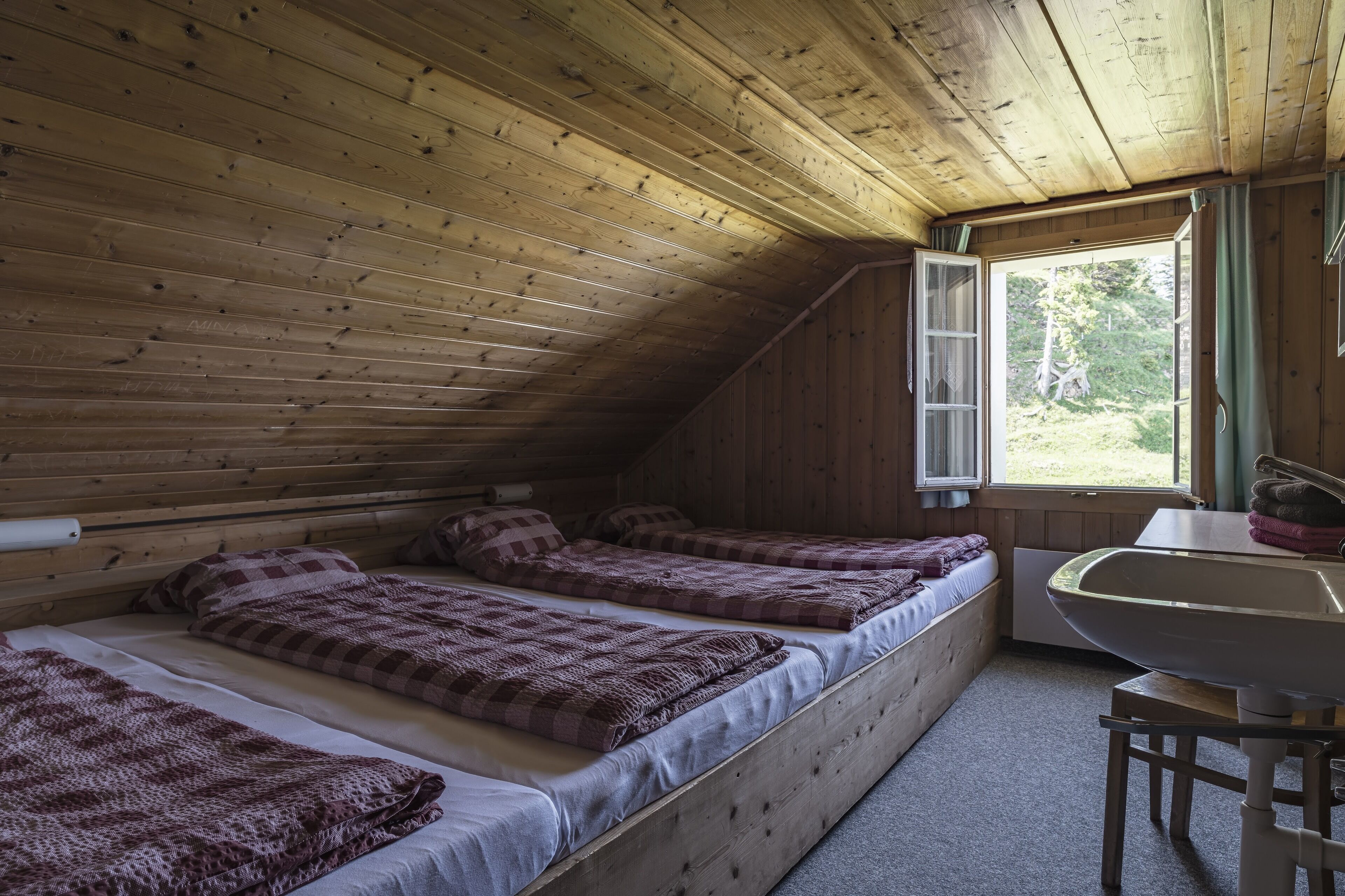 Une cabine avec trois lits en bois, une fenêtre avec des rideaux et un lavabo.