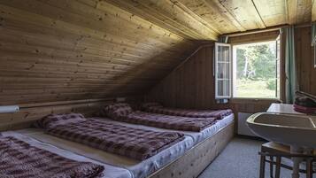Une cabine avec trois lits en bois, une fenêtre avec des rideaux et un lavabo.