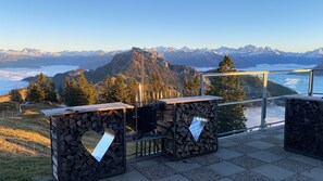 A terrace with a mountain view, stone tables, and a glass railing. - Rigi Burggeist Guesthouse (Gersau)