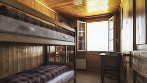 Habitación con literas, escritorio, silla, paredes de madera y ventana.