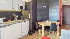 Une cuisine moderne équipée d’un four à micro-ondes, d’un évier et d’un lave-vaisselle. On y trouve une table ronde en bois, des chaises et un banc rouge.