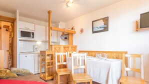A compact room with a dining table set for four, wooden chairs, a small kitchen area with a microwave, and a bed with a red blanket. - Renovated 2-room apartment, 6 people, southwest balcony, La Rosière (La Rosière)