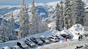 A snow-covered parking area with cars and people, surrounded by snow-laden trees and mountains in the background. - Renovated bright studio, balcony, near slopes, parking included (La Rosière)