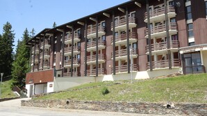 A multi-story hotel with balconies, a stone retaining wall, and a small parking area. - Renovated bright studio, balcony, near slopes, parking included (La Rosière)