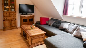 A living room with a wooden cabinet, a television, a grey sofa with cushions, and a wooden coffee table.