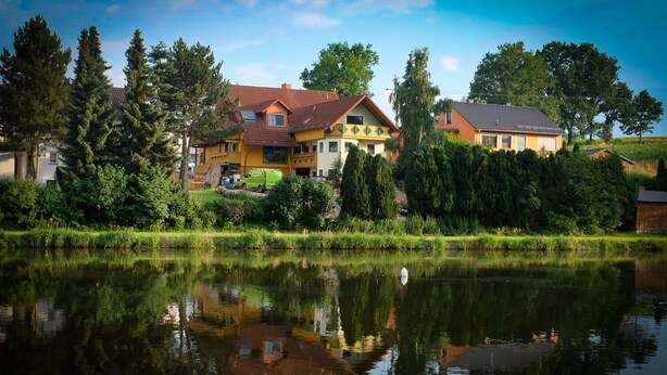 A lakeside property with a house featuring a red roof, a yellow facade, and a visible garage.