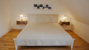 A bedroom with a large bed, wooden floor, two bedside tables with lamps, and a wall-mounted picture above the bed.