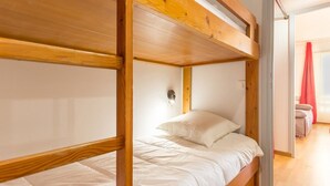 Une chambre avec un lit superposé, dont la structure est en bois et dont la literie est blanche.