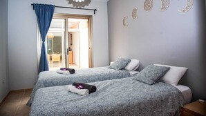 Ein Schlafzimmer mit zwei Betten, einem großen Fenster mit blauen Vorhängen und Mond-Wandbildern.