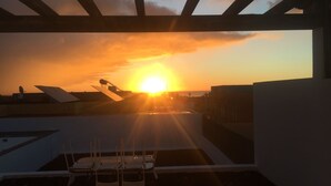 Eine Dachterrasse mit Blick auf den Sonnenuntergang über dem Meer, ausgestattet mit einer Pergola und mehreren Stühlen.