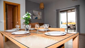 Ein Essbereich mit einem Holztisch, gedeckt für vier Personen, einer Blumenvase und Blick ins Freie durch ein großes Fenster.