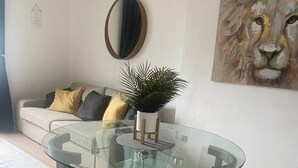 A modern living room with a glass table, a sofa with cushions, a potted plant, and a framed artwork on the wall. - Lovely 1-bed Apartment in London - View of Shard (London)