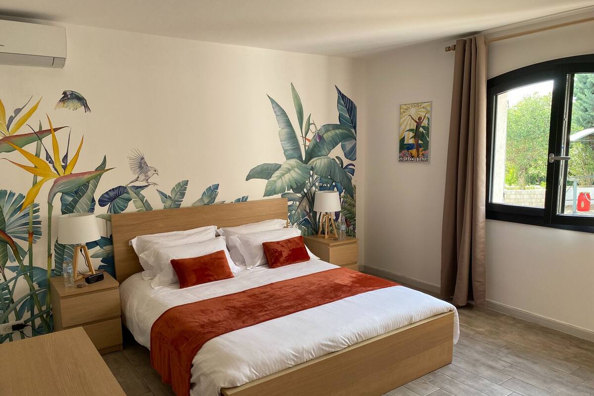 Una habitación de hotel con una cama, una mesita de noche, una lámpara y una ventana con cortinas.