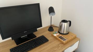 Un bureau en bois, sur lequel se trouvent un écran noir, un clavier et une bouilloire en acier inoxydable.