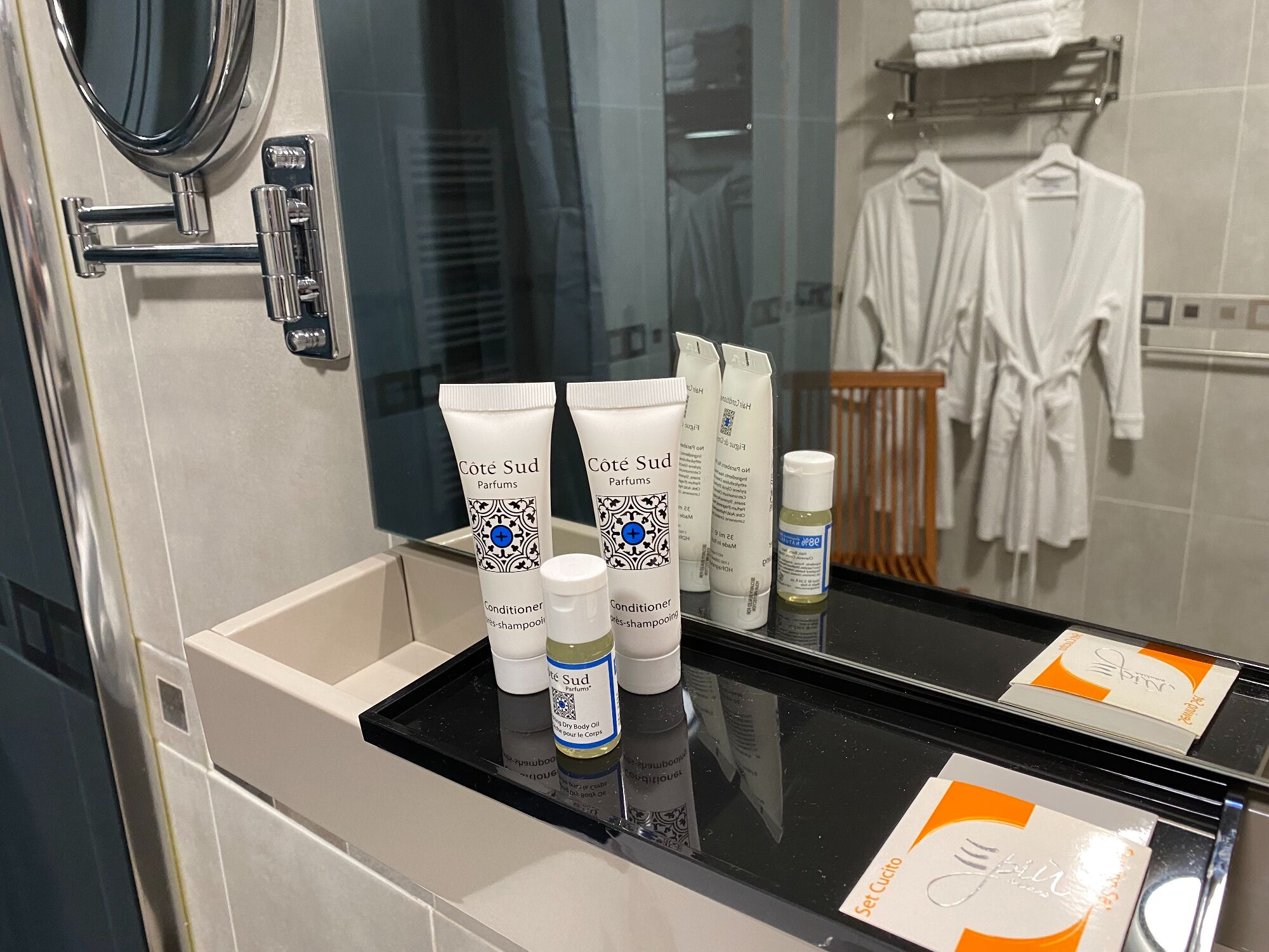 A bathroom with toiletries on a counter, a mirror, and a rack of white robes.