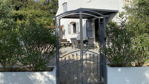Een wit gebouw met een overdekte patio, een metalen hek en omliggend groen.