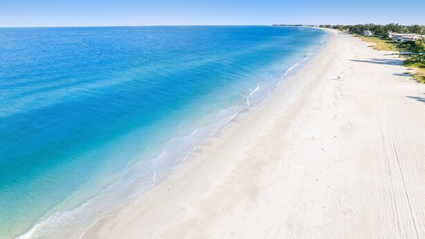 A wide, sandy beach with clear blue water and a few buildings in the distance. - Seahorse and Starfish by Beach Boutique Rentals (Bradenton Beach)