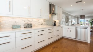A modern kitchen with white cabinetry, a tiled backsplash, and wooden flooring. - Seahorse and Starfish by Beach Boutique Rentals (Bradenton Beach)