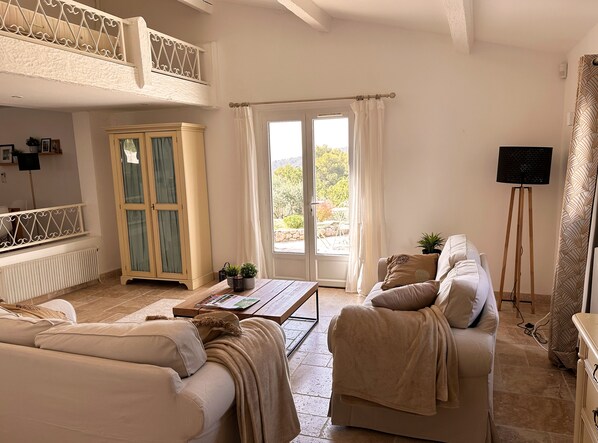 A cozy living room with a sofa, a coffee table, and a cabinet. There is a balcony with a view of the outdoors.
