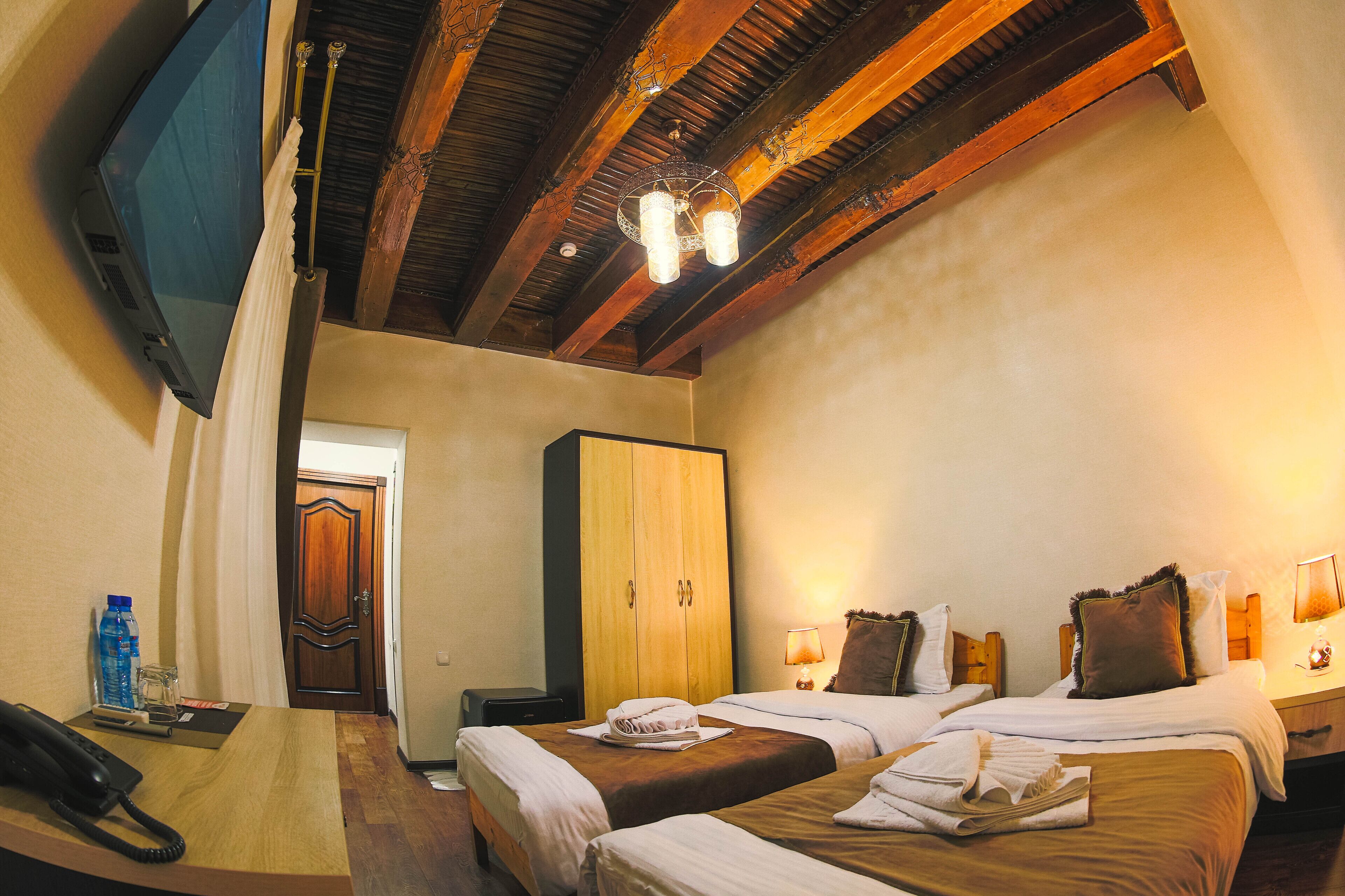 Habitación de hotel con dos camas, un armario de madera, un televisor y un teléfono sobre el escritorio.