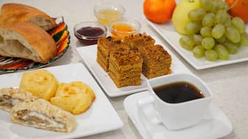 A table with bread, pastries, fruit, and condiments.