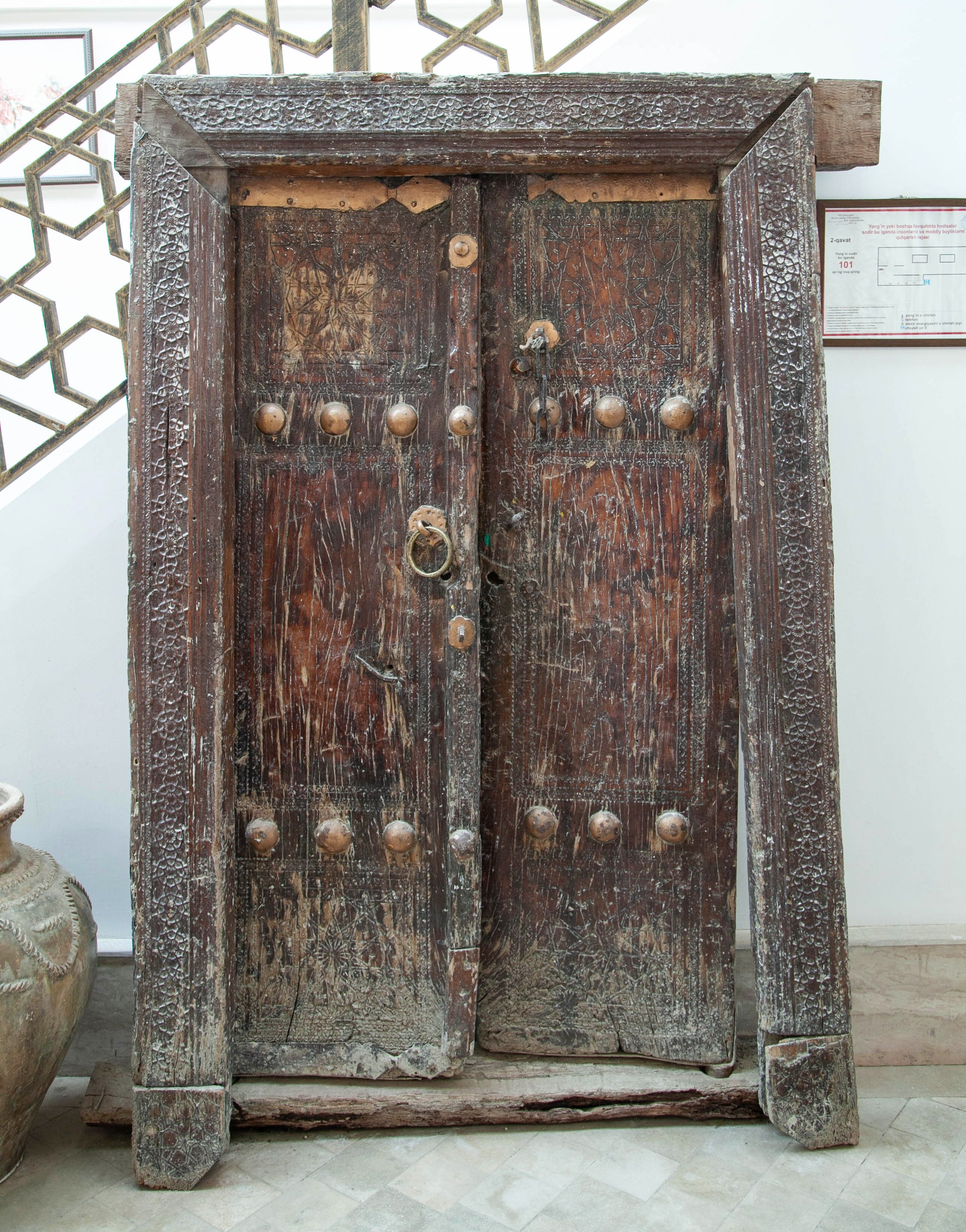 Una antigua puerta de madera con remaches metálicos y un cerrojo, frente a un patrón geométrico en la pared.