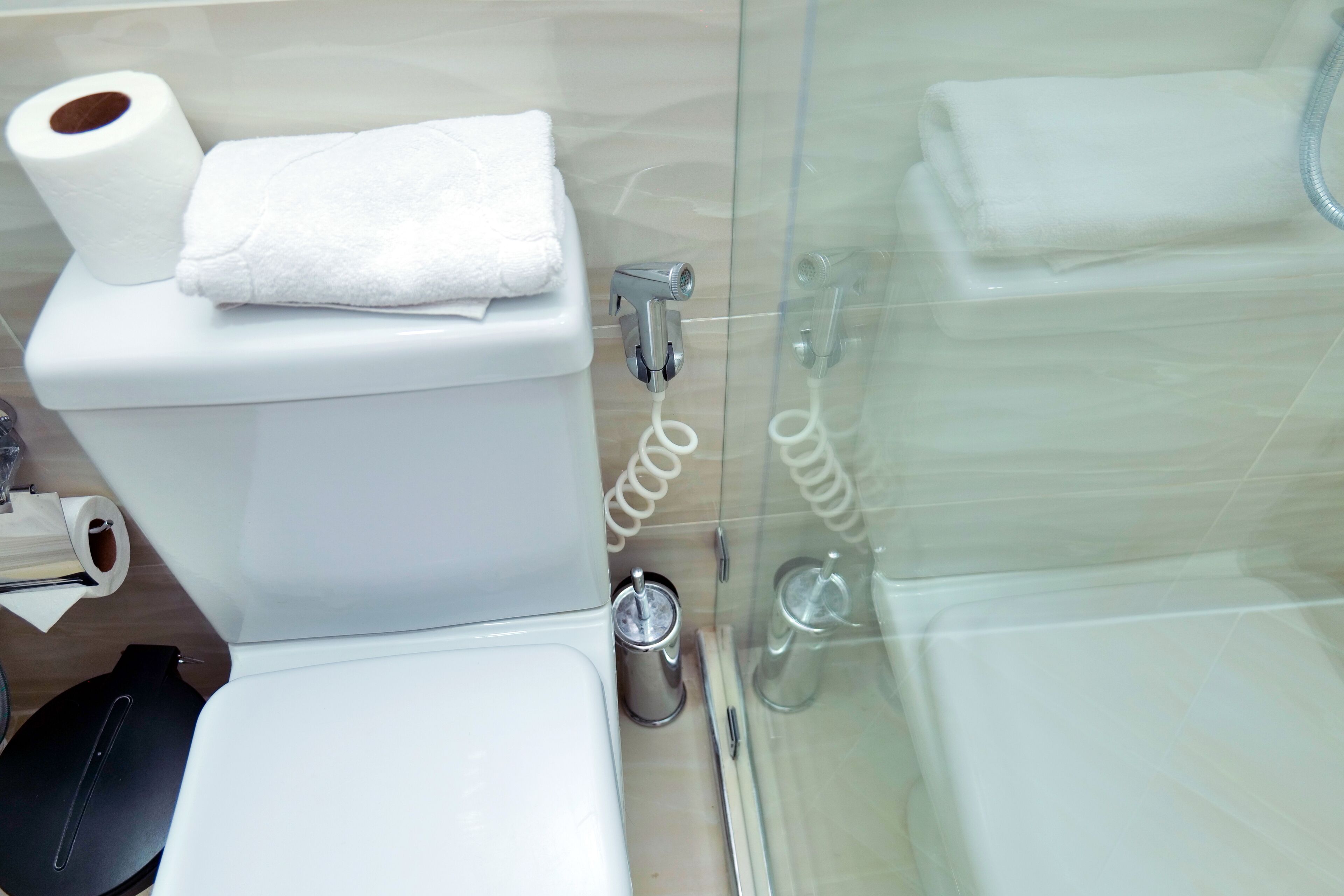 Un baño con inodoro, cabina de ducha de vidrio y una toalla sobre el tanque.