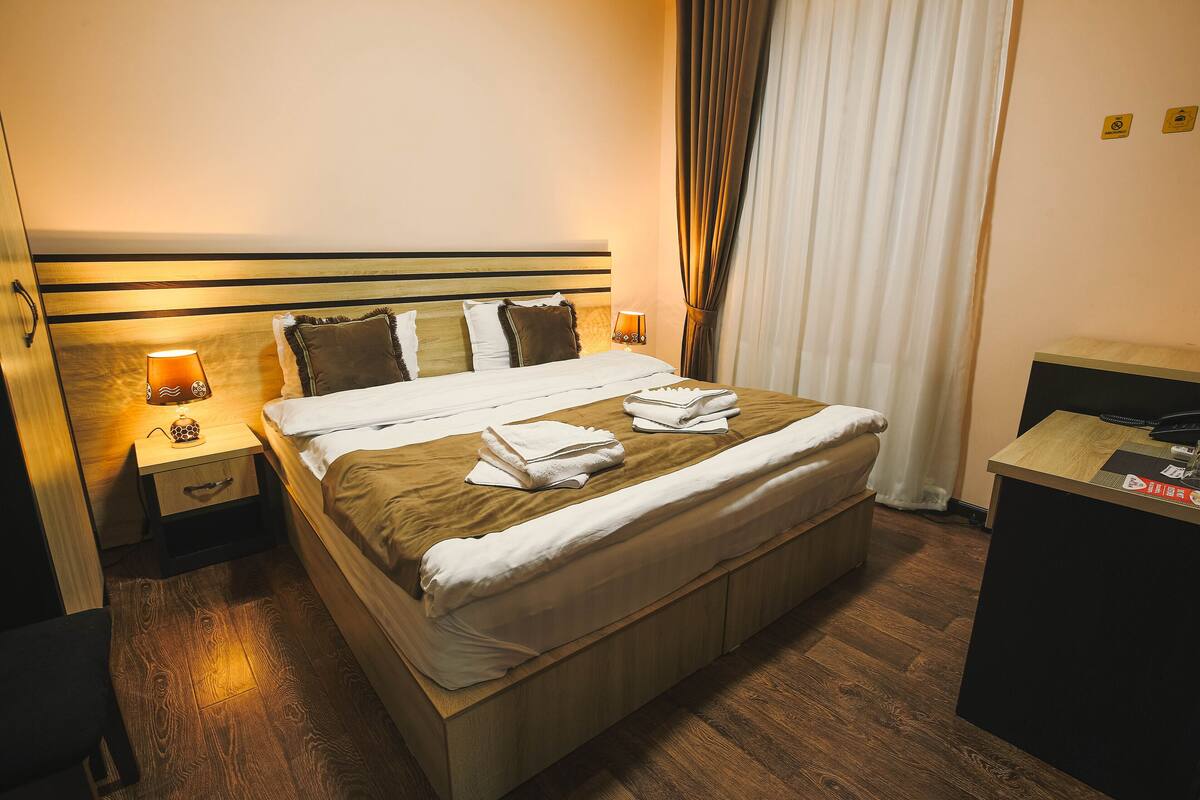 A neatly made bed with white linens, a bedside table with a lamp, and a desk with a computer.