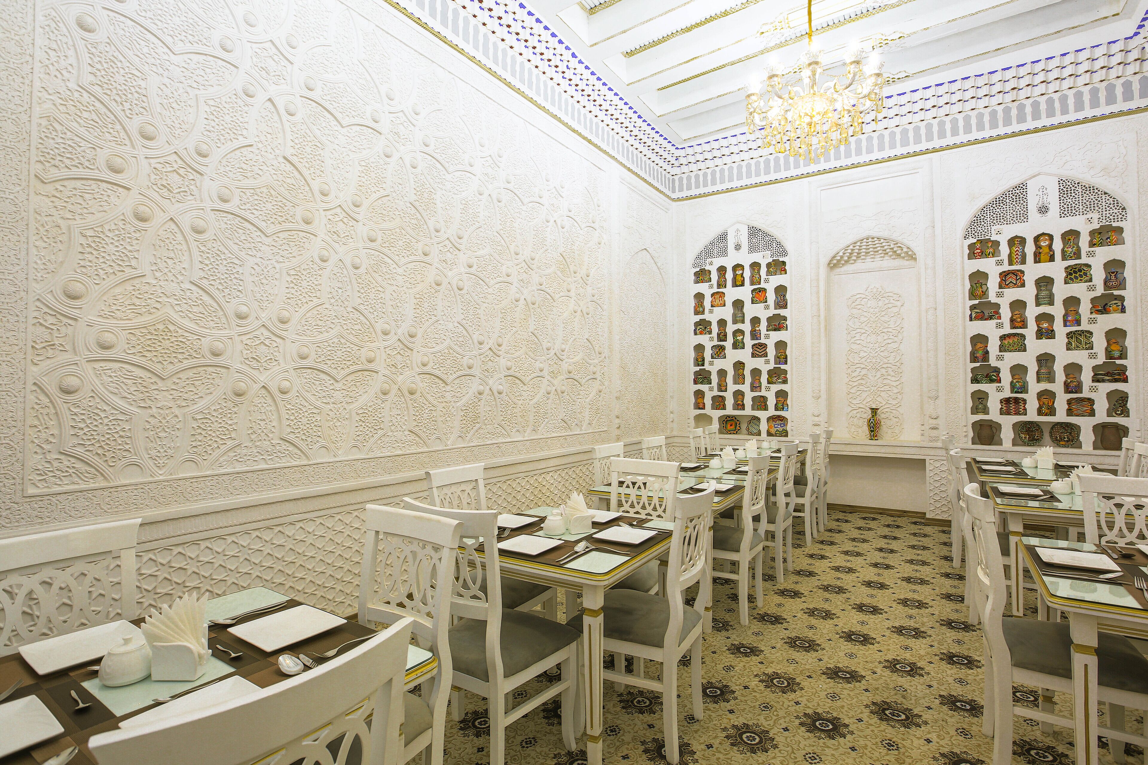 A dining area with white ornate walls, chandeliers, and patterned floor tiles.