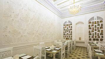 A dining area with white ornate walls, chandeliers, and patterned floor tiles.