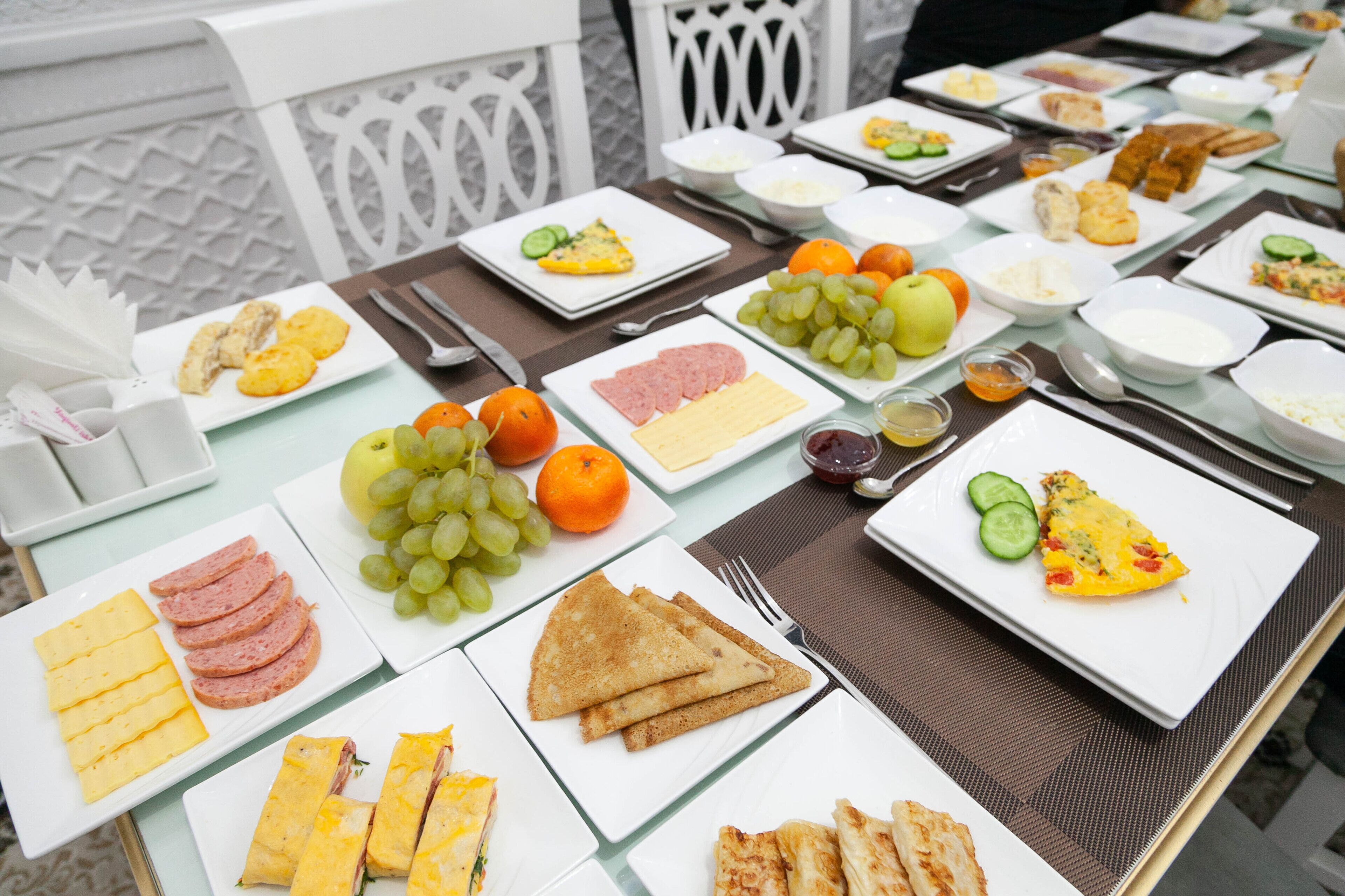 Una mesa dispuesta con diferentes alimentos para el desayuno, como huevos, jamón, queso, tostadas y frutas.