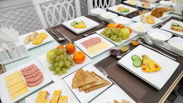 Een gedekte tafel met diverse ontbijtartikelen, waaronder eieren, ham, kaas, toast en fruit.