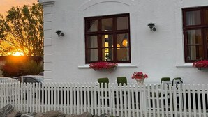 Un edificio blanco con varias ventanas, una cerca blanca de piquetes y un muro de piedra.