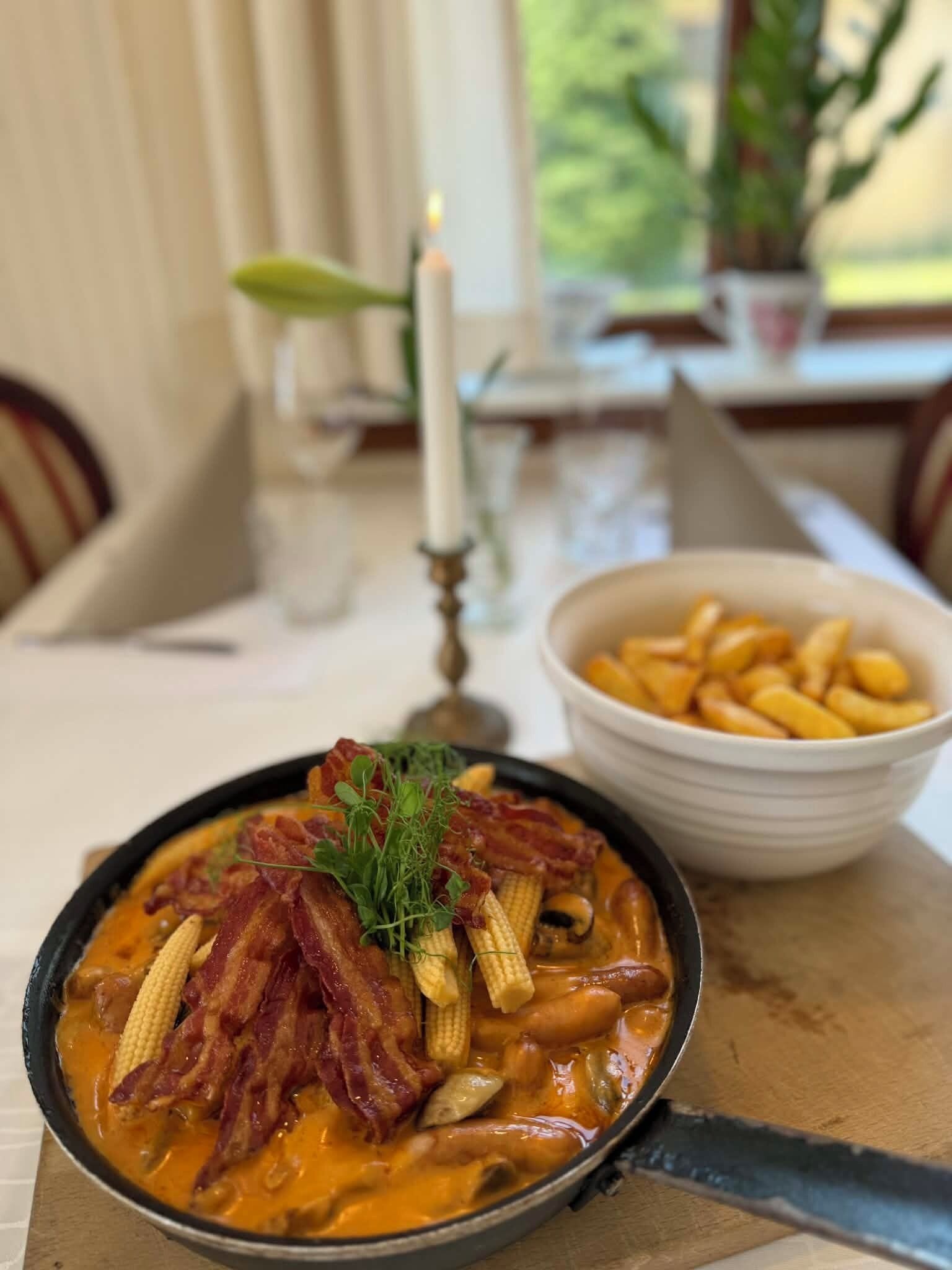 A bowl of food with bacon and corn on a table.