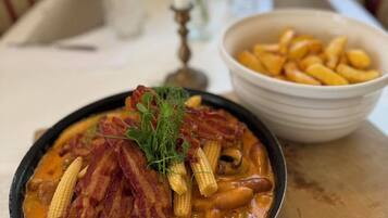 A bowl of food with bacon and corn on a table.