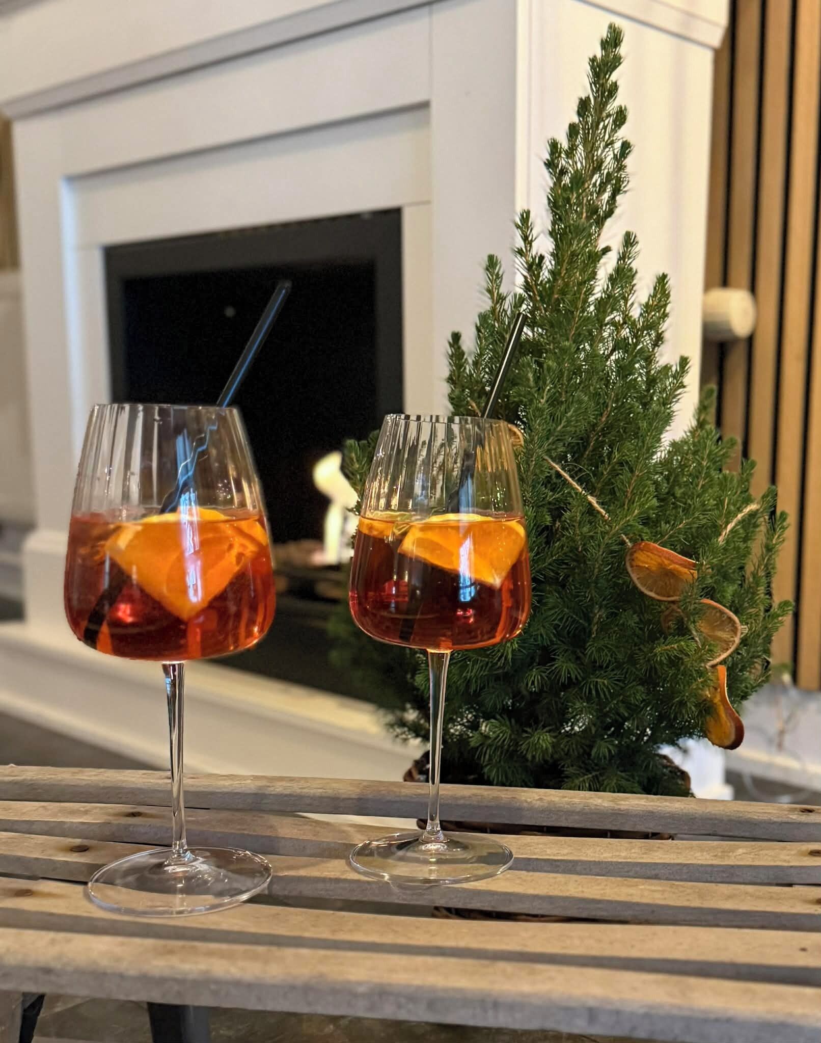 Two glasses of amber-colored beverage on a wooden table with a Christmas tree in the background.