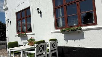 A white building with 'HUMBLE KRO' signage, two windows with wooden frames, a white picket fence, and outdoor seating with green cushions.
