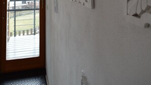 A room with a wooden door leading to a balcony, white decorative wall panels, and a view of a house and mountains in the background.