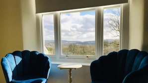 Una habitación con dos sillas azules y una pequeña mesa junto a una ventana que ofrece vistas a un paisaje.