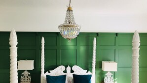 Un dormitorio con cama con dosel, paredes cubiertas de paneles verdes, una araña y mesitas de noche con lámparas.