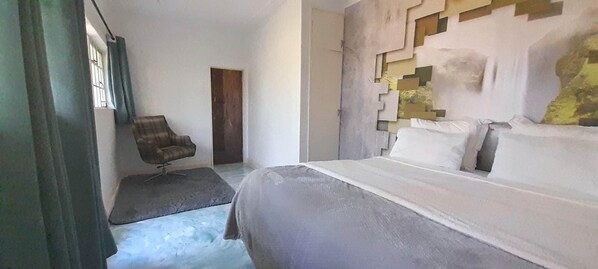 A bedroom with a bed, a chair, and a wall with geometric patterns. - Zebras Dazzle B&B | Room 24 | Fresh, light & natural (Chinhoyi)