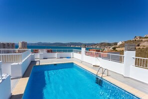 A rooftop swimming pool with a clear view of the sea and distant mountains.