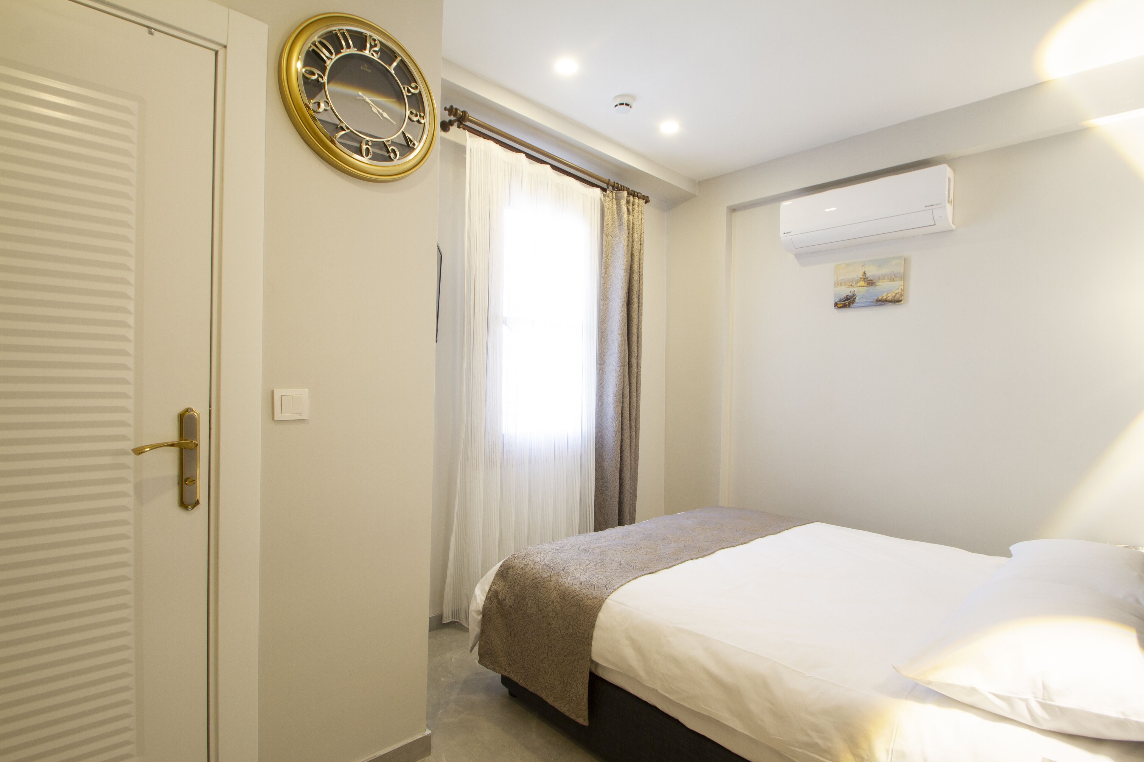 A hotel room with a bed, a clock, an air conditioning unit, and a window with curtains.