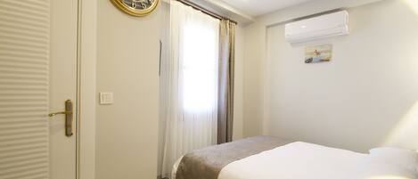 A hotel room with a bed, a clock, an air conditioning unit, and a window with curtains.
