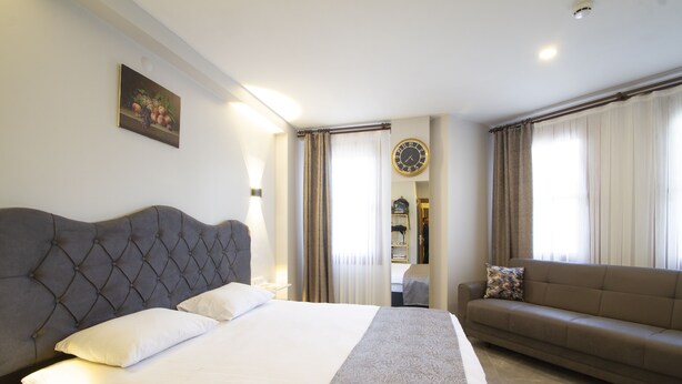 Una camera d'albergo con un letto grande, un divano, una sveglia a muro e un quadro.