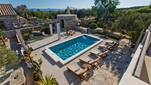 A rectangular swimming pool with lounge chairs and a stone chimney. - Pet friendly home in Bogomolje (Bogomolje)
