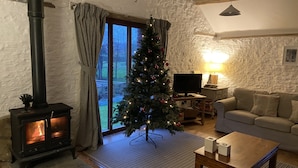 A cozy living room with a fireplace, a Christmas tree, a sofa, and a television. - Beautiful Barn Conversion With Wood-burning Stove (Yeovil)