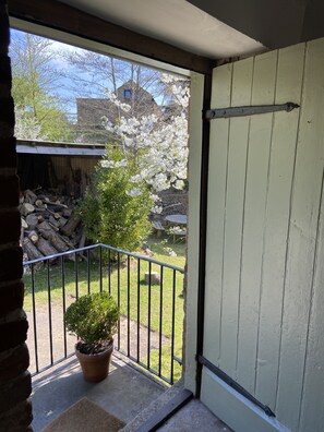 Ein Balkon mit einem Blumentopf, einem Holzzaun und Blick auf einen Hinterhof mit Holzstapel und einem Haus im Hintergrund.